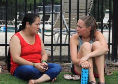 Two women sitting on the grass talking to each other.