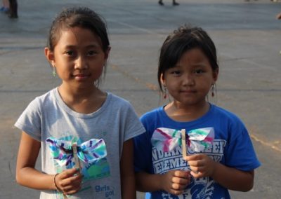 Two young girls holding up paper kites in front of a building.