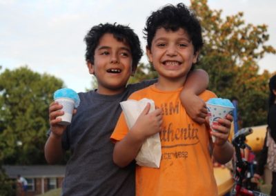 Two boys holding cups of ice cream and smiling.